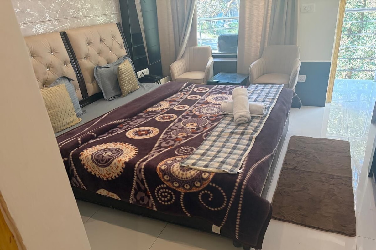 Ein Schlafzimmer mit einem großen Bett, einer Couch, zwei Sesseln, einem kleinen Tisch und Blick ins Freie.