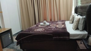 A hotel room with a bed, a desk, and a window with curtains. - Mirage Grand (Dharamshala)