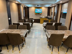 A conference room with tables and chairs, a television screen, and a podium with a microphone. - Mirage Grand (Dharamshala)