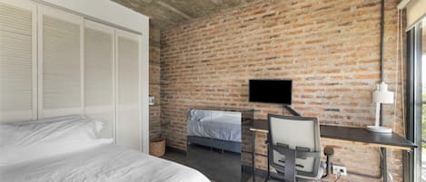 Un dormitorio con una cama grande, un escritorio con computadora, un televisor y una pared de ladrillo.