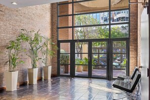 A spacious lobby with a large glass door leading to an outdoor area, featuring a brick wall and several potted plants. - Fabulous & stylish apartment in Palermo Hollywood (Buenos Aires)