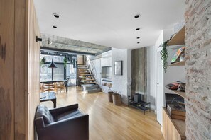 Ein zeitgemäßer Wohnraum mit Holzboden, einem schwarzen Ledersofa, einer Treppe und einer Küchenzeile mit an der Wand befestigtem Fernseher.