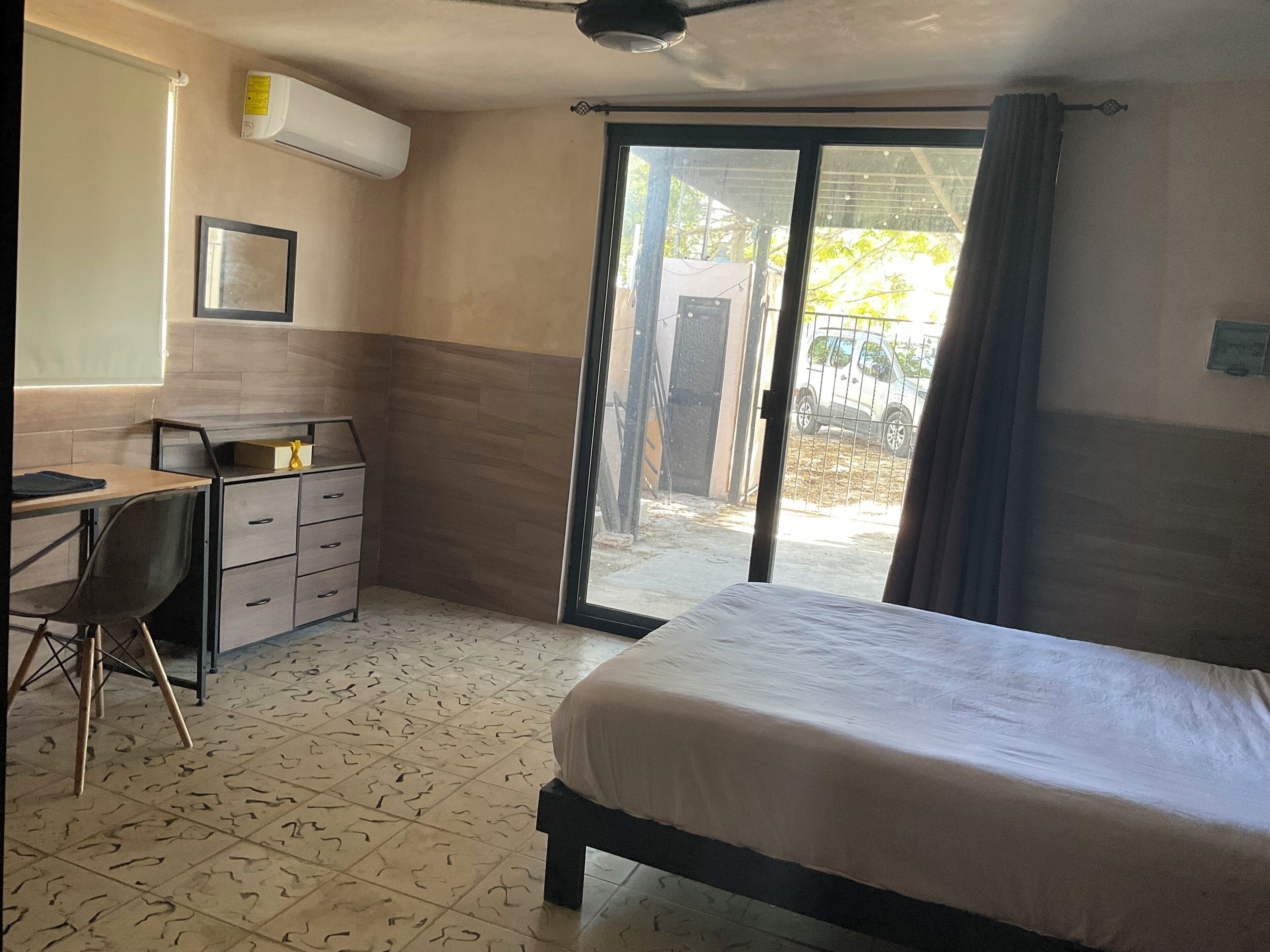 A room with a bed, a desk, a chair, a wardrobe, and a sliding glass door leading to an outdoor area.