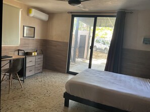 Une chambre comprenant un lit, un bureau, une chaise, une armoire et une porte-fenêtre coulissante donnant sur un espace extérieur.