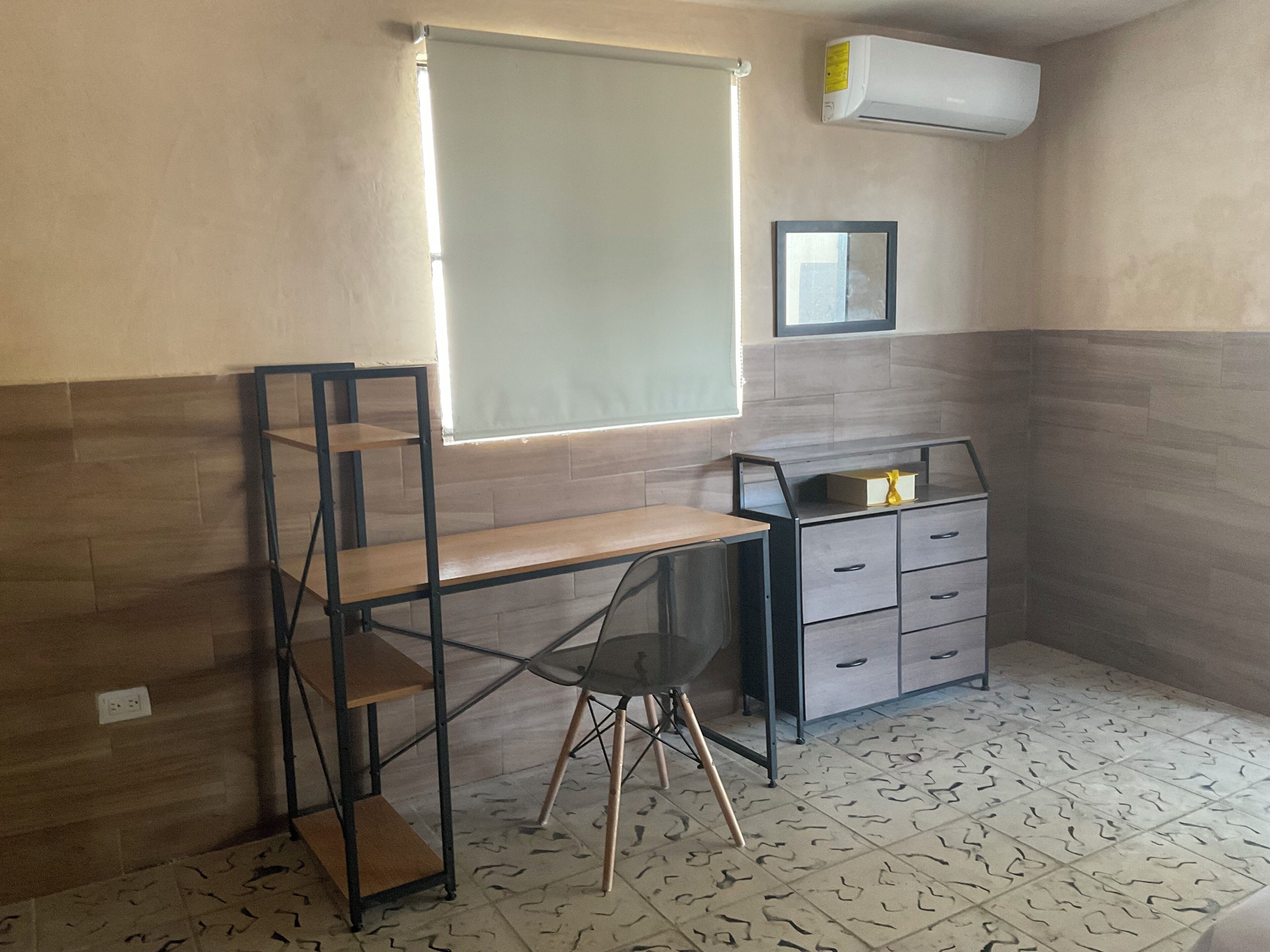 A room with a desk, a chair, a shelf unit, a cabinet, and a window with blinds.