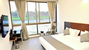 Et hotelværelse med seng, skrivebord, stol, fjernsyn og et vindue med gardiner.