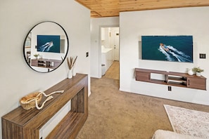 Ein Wohnzimmer mit einem großen, an der Wand befestigten Fernseher, einem Holzkonsolentisch und einem Spiegel.