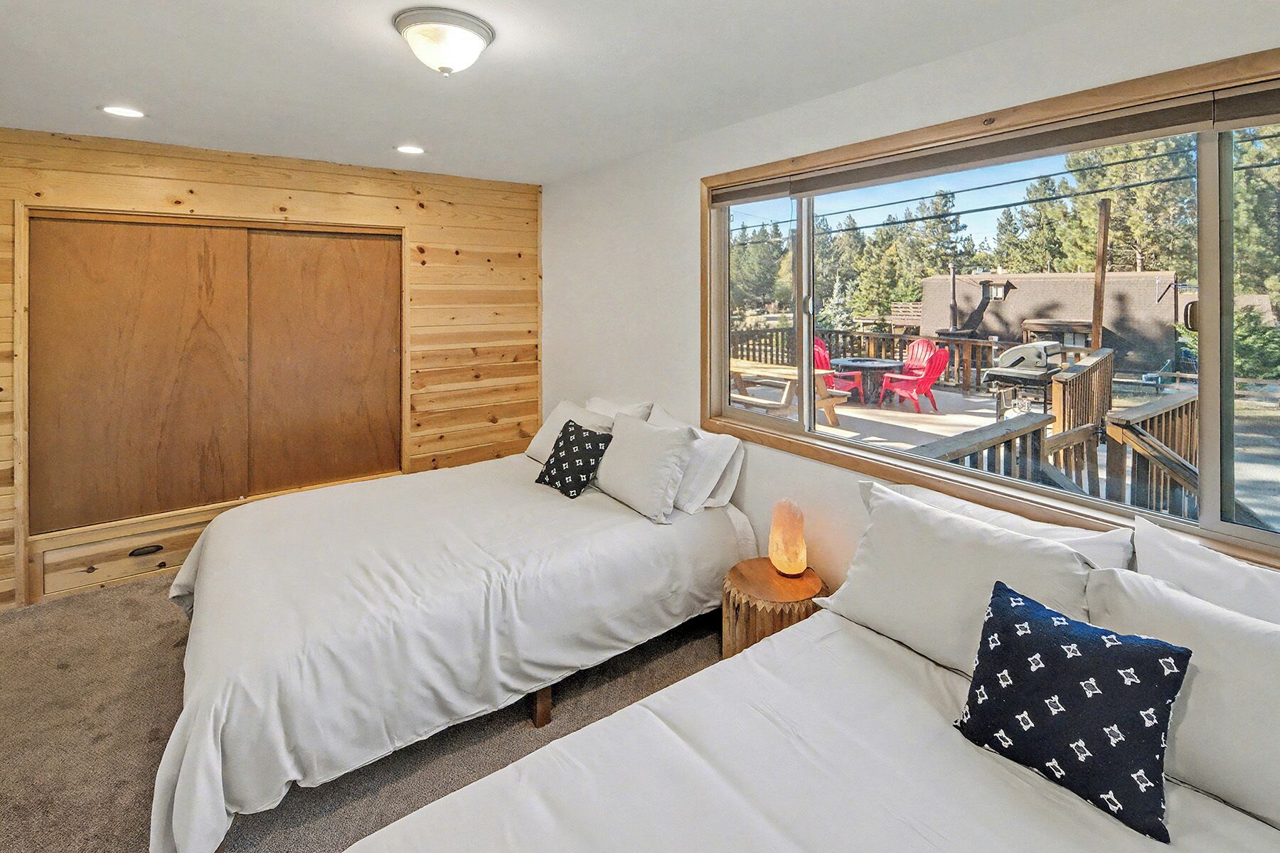 A room with two beds, a wooden wardrobe, and a large window with a view of outdoor seating.