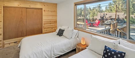 A room with two beds, a wooden wardrobe, and a large window with a view of outdoor seating.
