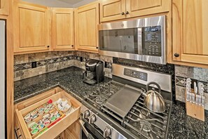 Una cocina con armarios de madera, un microondas de acero inoxidable, una cafetera y una estufa.