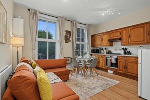 Eine moderne Küche mit Holzausstattung, ein Essbereich mit Tisch und Stühlen sowie ein Wohnzimmer mit Sofa und Lampe.