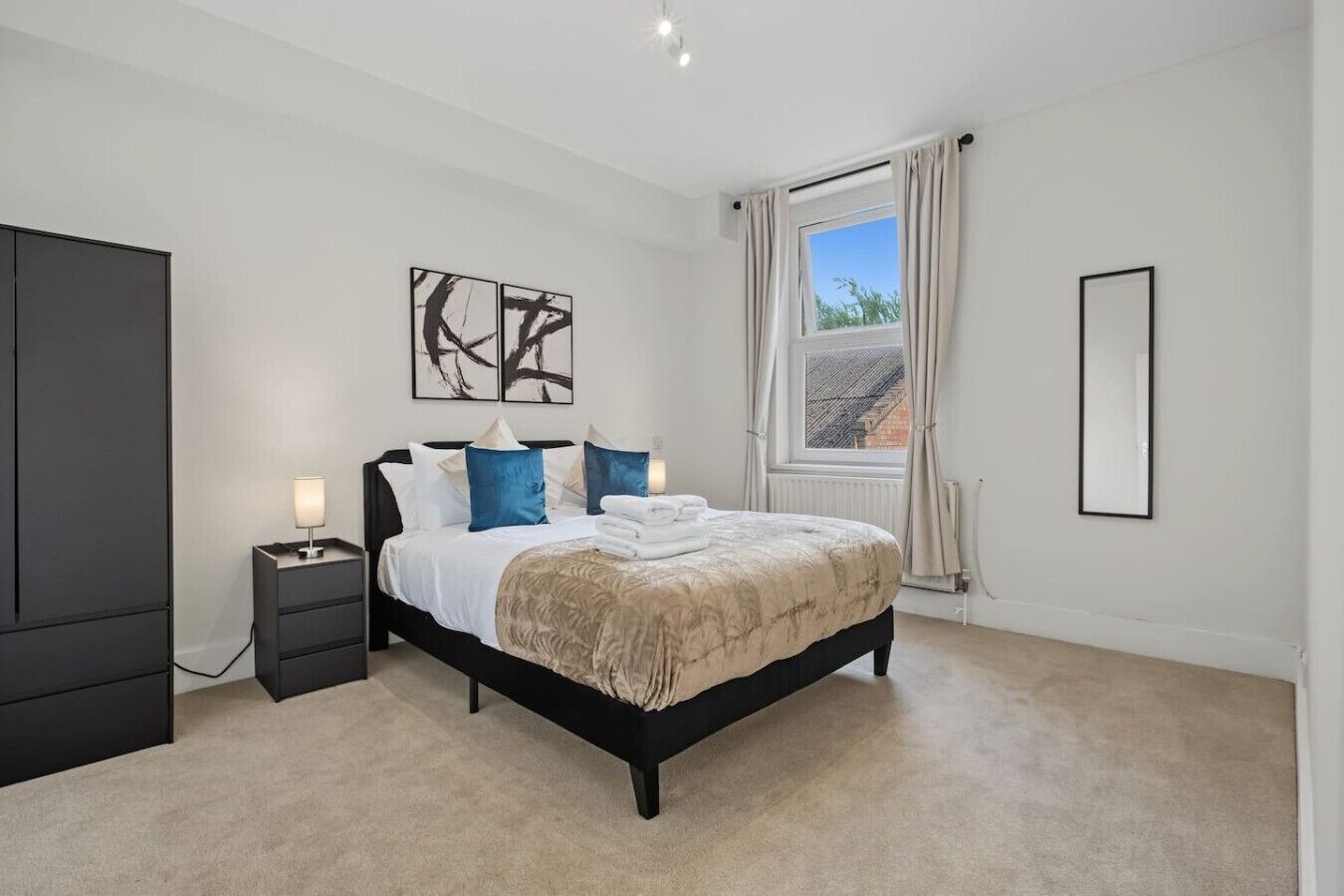 A bedroom with a bed, bedside tables, a window with curtains, and artwork on the wall.