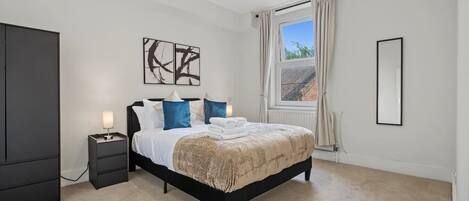 A bedroom with a bed, bedside tables, a window with curtains, and artwork on the wall.