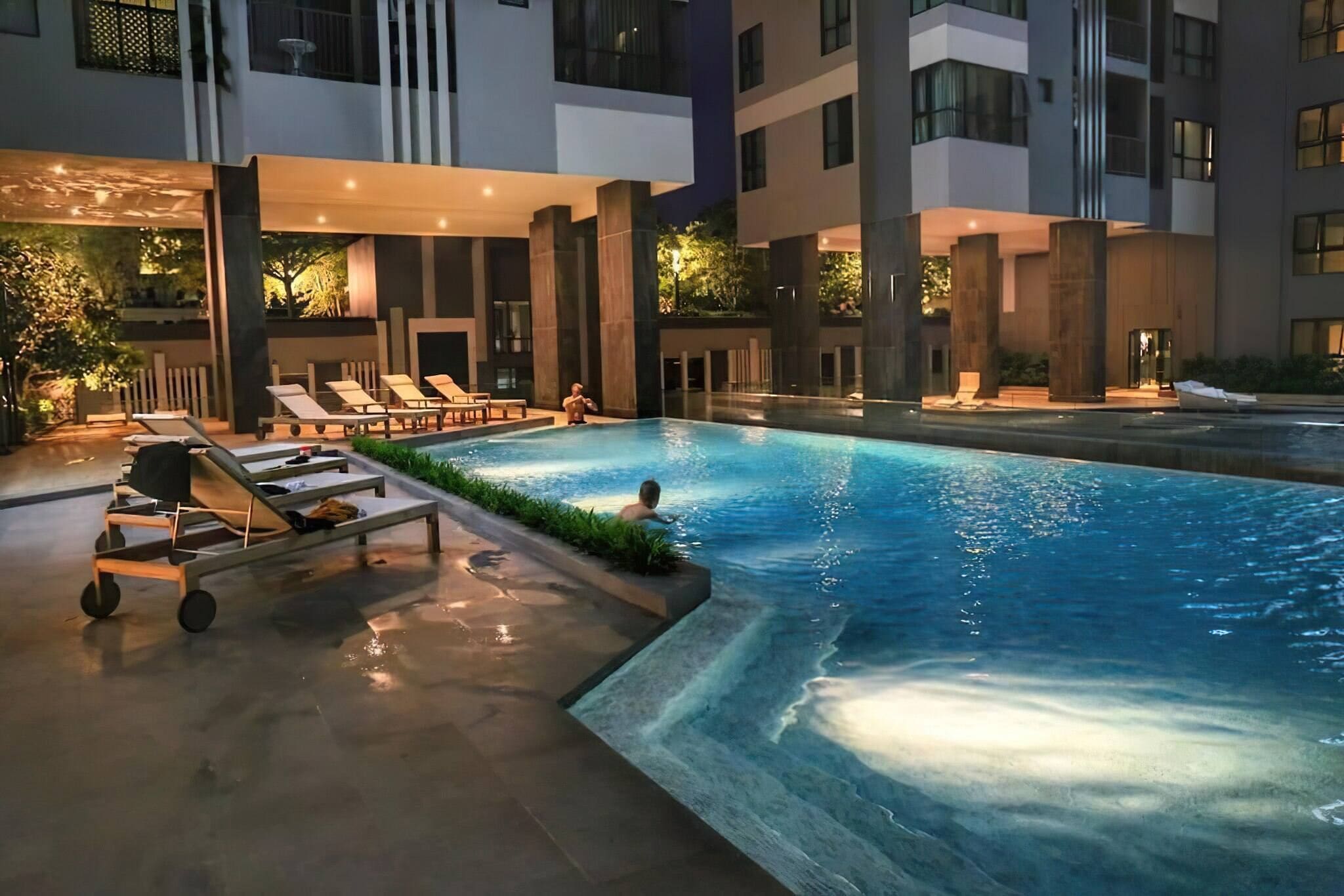 An outdoor swimming pool with lounge chairs and a poolside cart, surrounded by modern buildings.