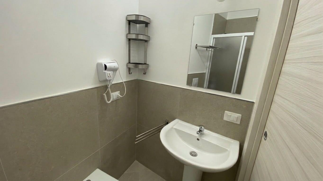 Ein Badezimmer mit Waschbecken, Spiegel, Handtuchhalter und Duschabtrennung.
