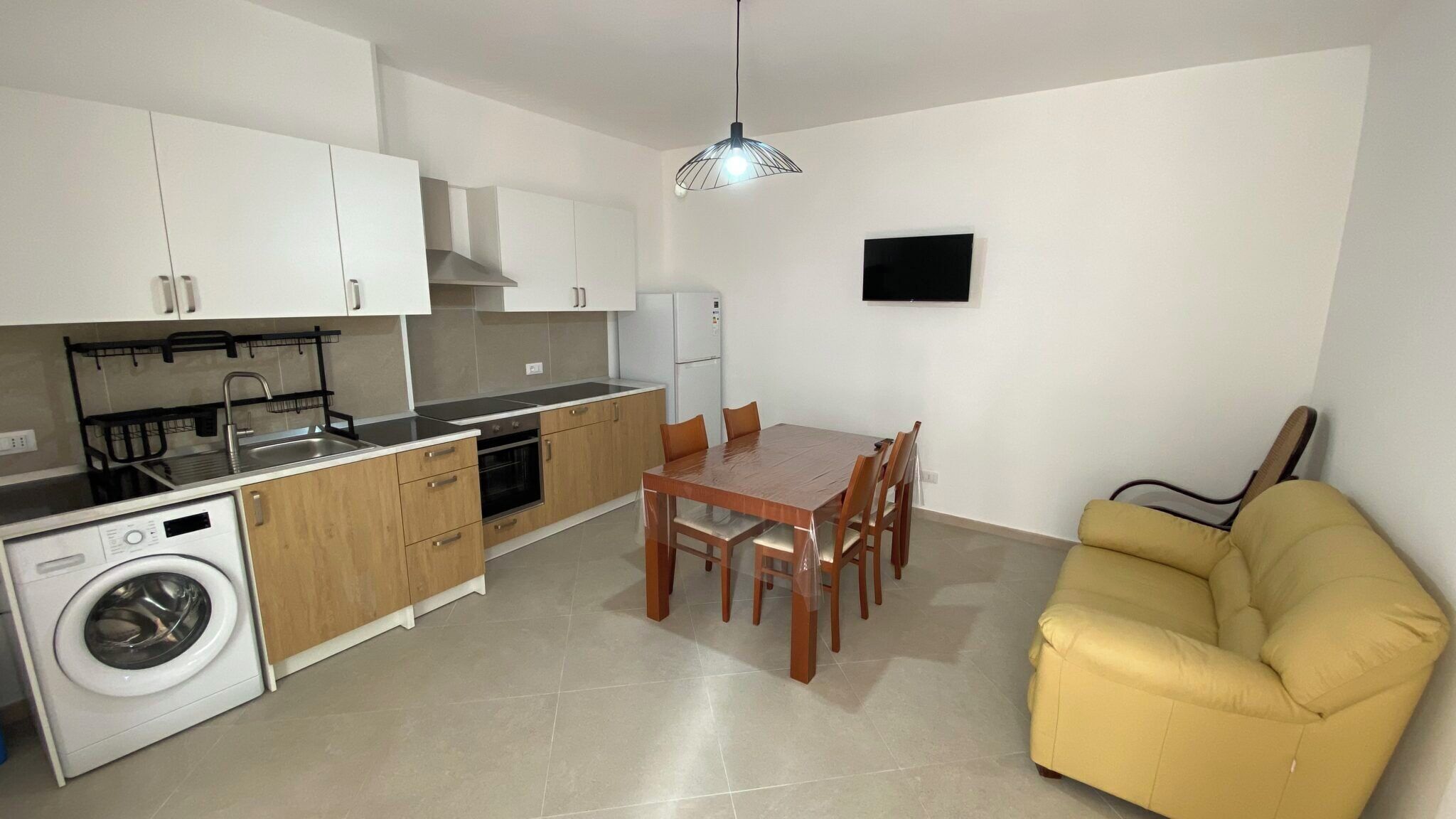 Eine kompakte Küche mit Waschmaschine, Holzschränken, einem Esstisch mit Stühlen und einem gelben Sofa.