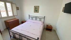 Ein Schlafzimmer mit Bett, Schminktisch, Nachttischen und einem Fenster mit Dekorglas.