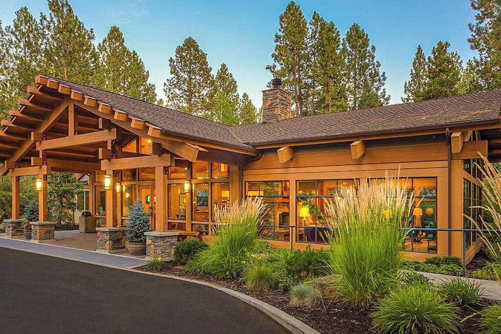 A lodge with a covered entrance, large windows, and a stone chimney.