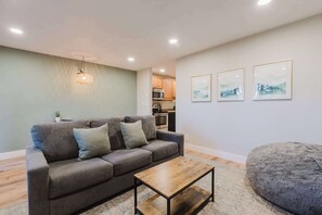 A living room with a sofa, a coffee table, a hanging light fixture, and a kitchen in the background. - Bend Adventure Starts Here - Near Mt Bachelor (Bend)