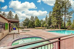 A swimming pool area with a hot tub, surrounded by trees and a building with a sign. - Bend Adventure Starts Here - Near Mt Bachelor (Bend)