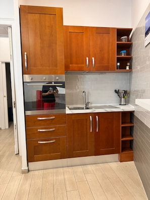 A compact kitchen with wooden cabinets, a stainless steel oven, a sink, and a tiled backsplash. - ALICJA HOUSE (Casoria)