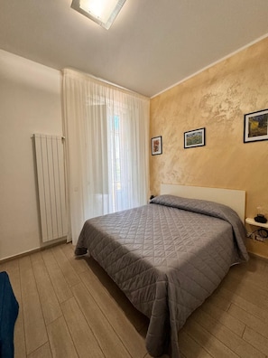 Ein Schlafzimmer mit einem Bett, einem Heizkörper, einem Fenster mit Vorhängen und zwei gerahmten Bildern an der Wand.