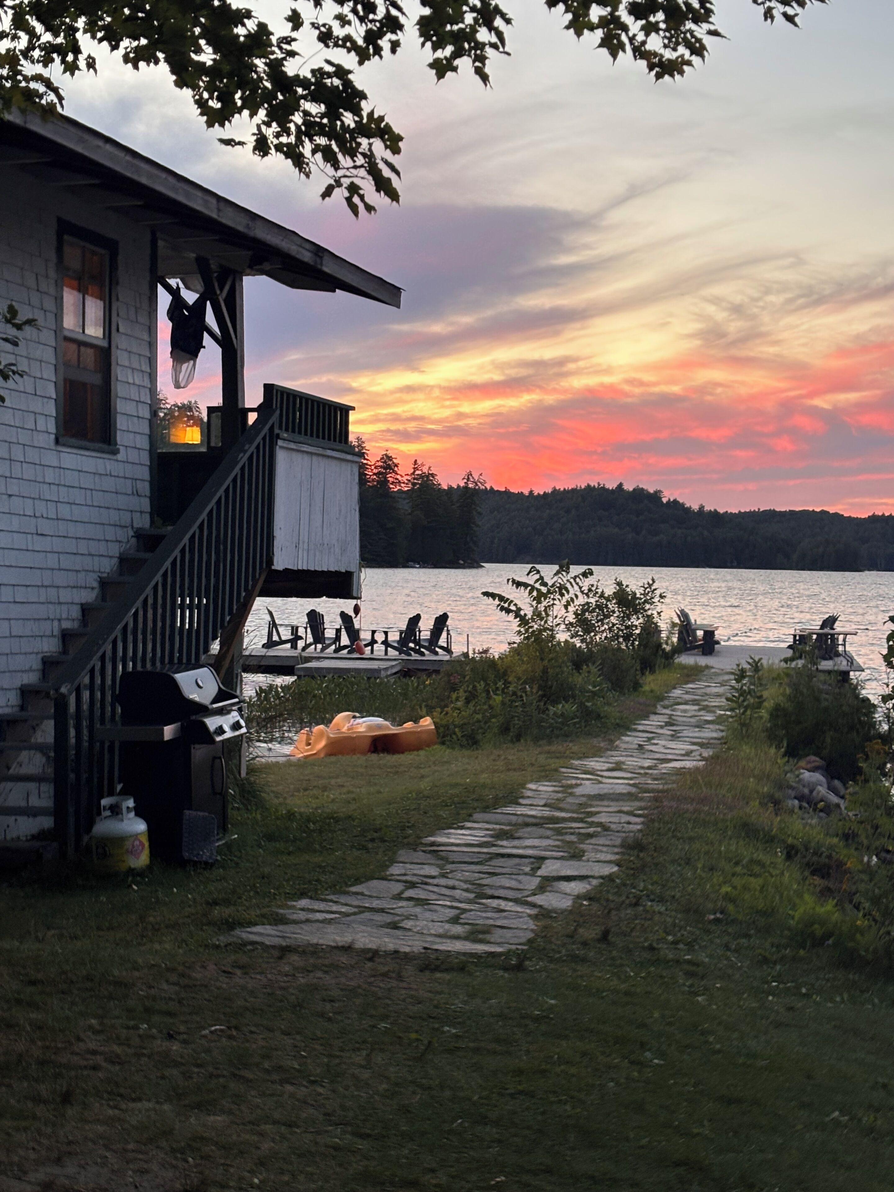 A lakeside cabin with a deck, outdoor seating, and a grill.