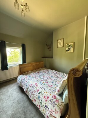 A bedroom with a bed, a window with curtains, a wall-mounted deer head decoration, and two framed pictures.