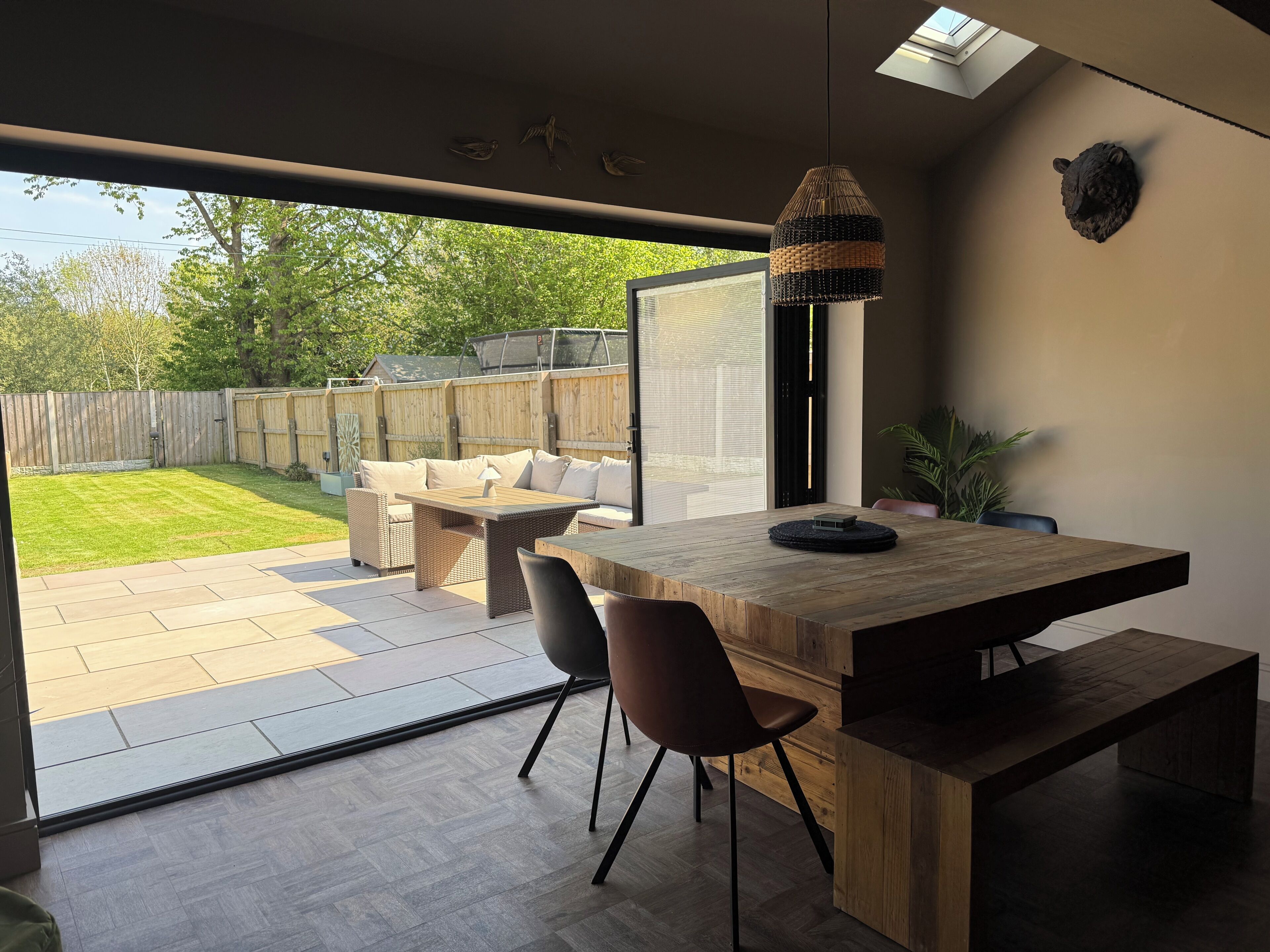 A modern patio with a dining area, a large window, and a view of the backyard.