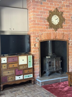 A room with a brick fireplace, a television on a cabinet, and a decorative clock on the wall. - Quirky canal side cottage pet friendly, walkable to pub/restaurant (Stanley)
