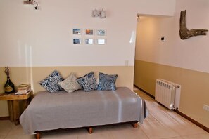 A bedroom with a bed, a nightstand, a wall-mounted light fixture, a radiator, and a wall-mounted piece of wood.