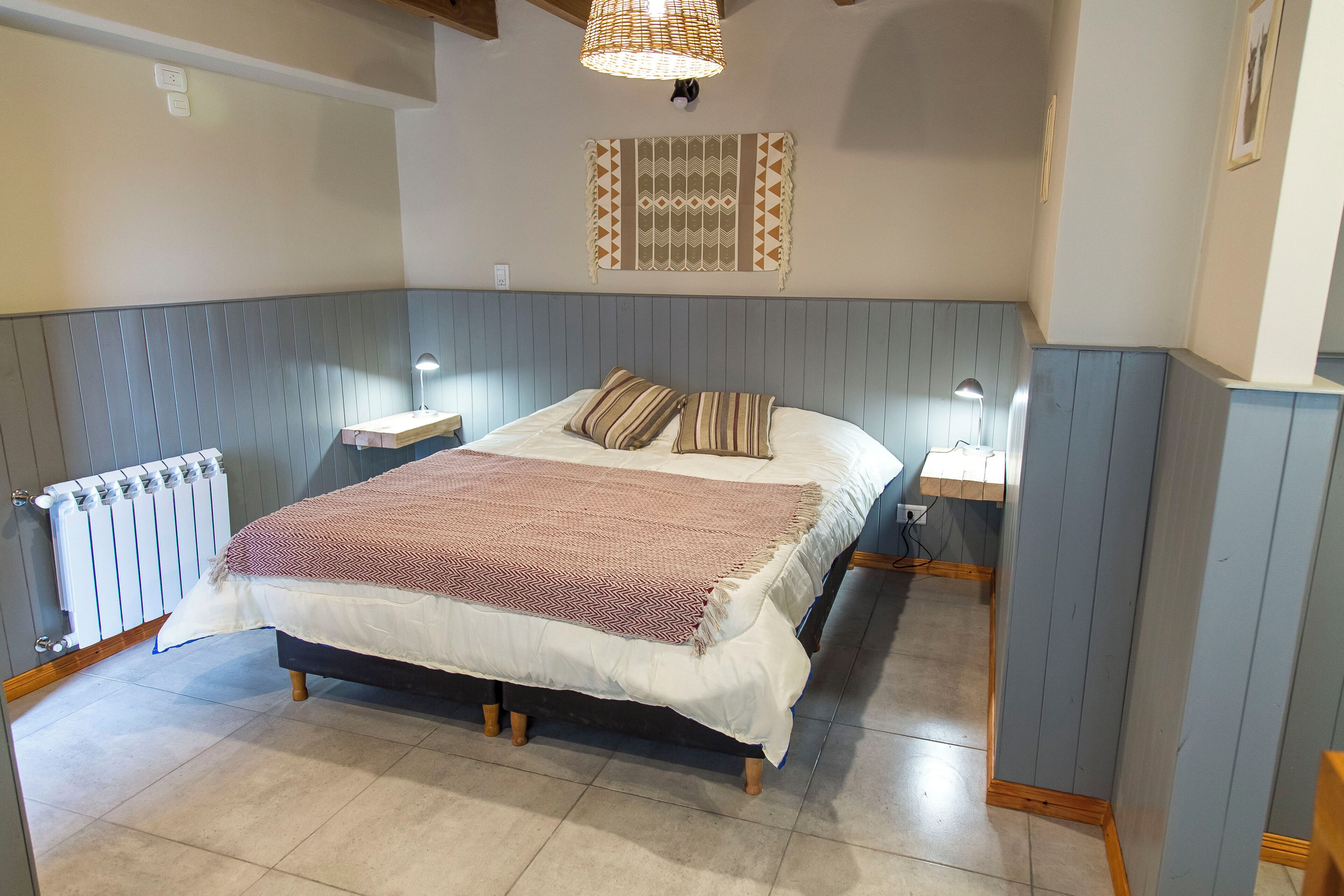 A bedroom with a bed, bedside lamps, a radiator, and a wall-mounted light fixture.