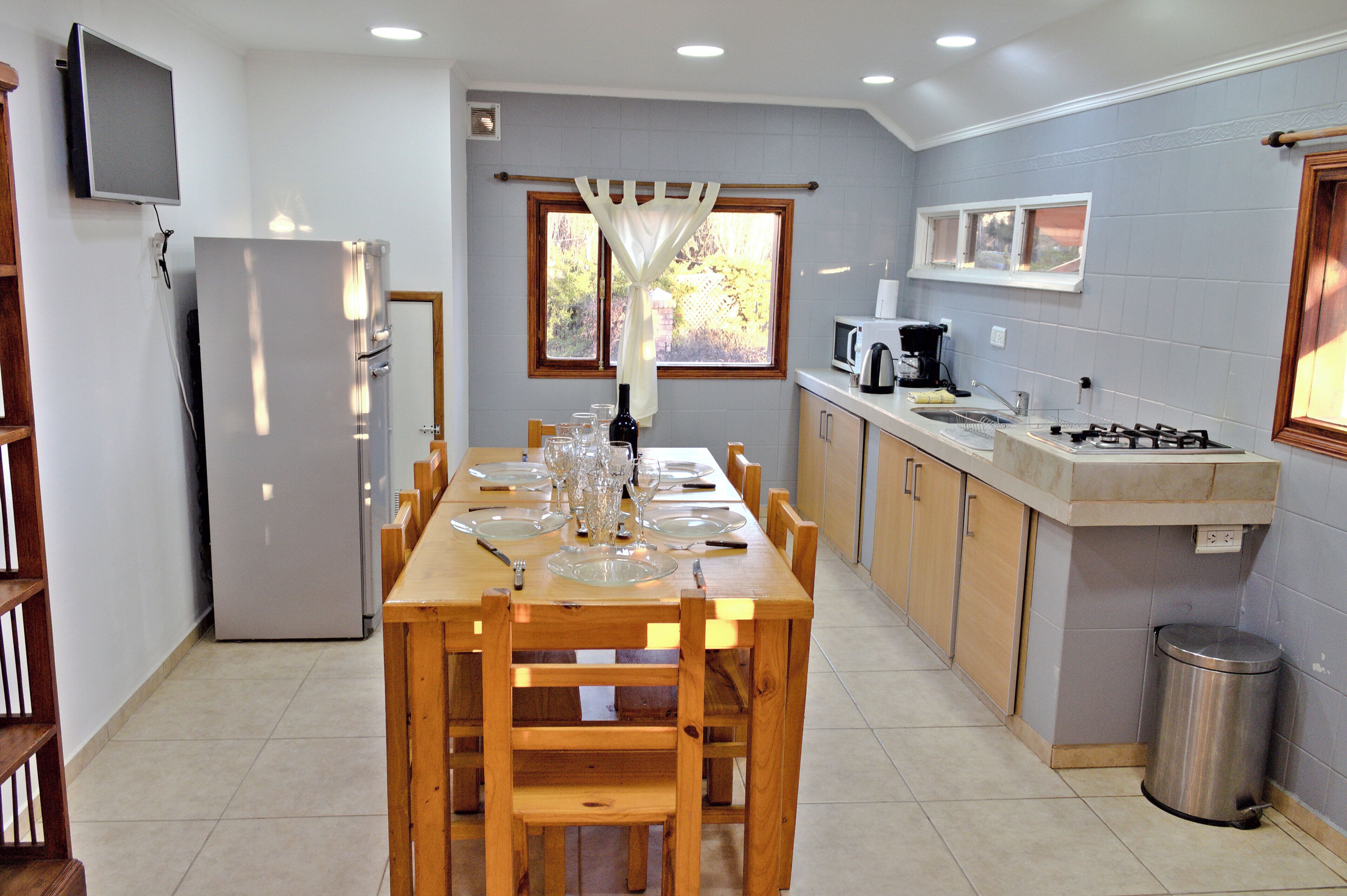 Una cocina con una mesa de comedor lista para seis personas, un refrigerador, un microondas, una cafetera y un lavaplatos.