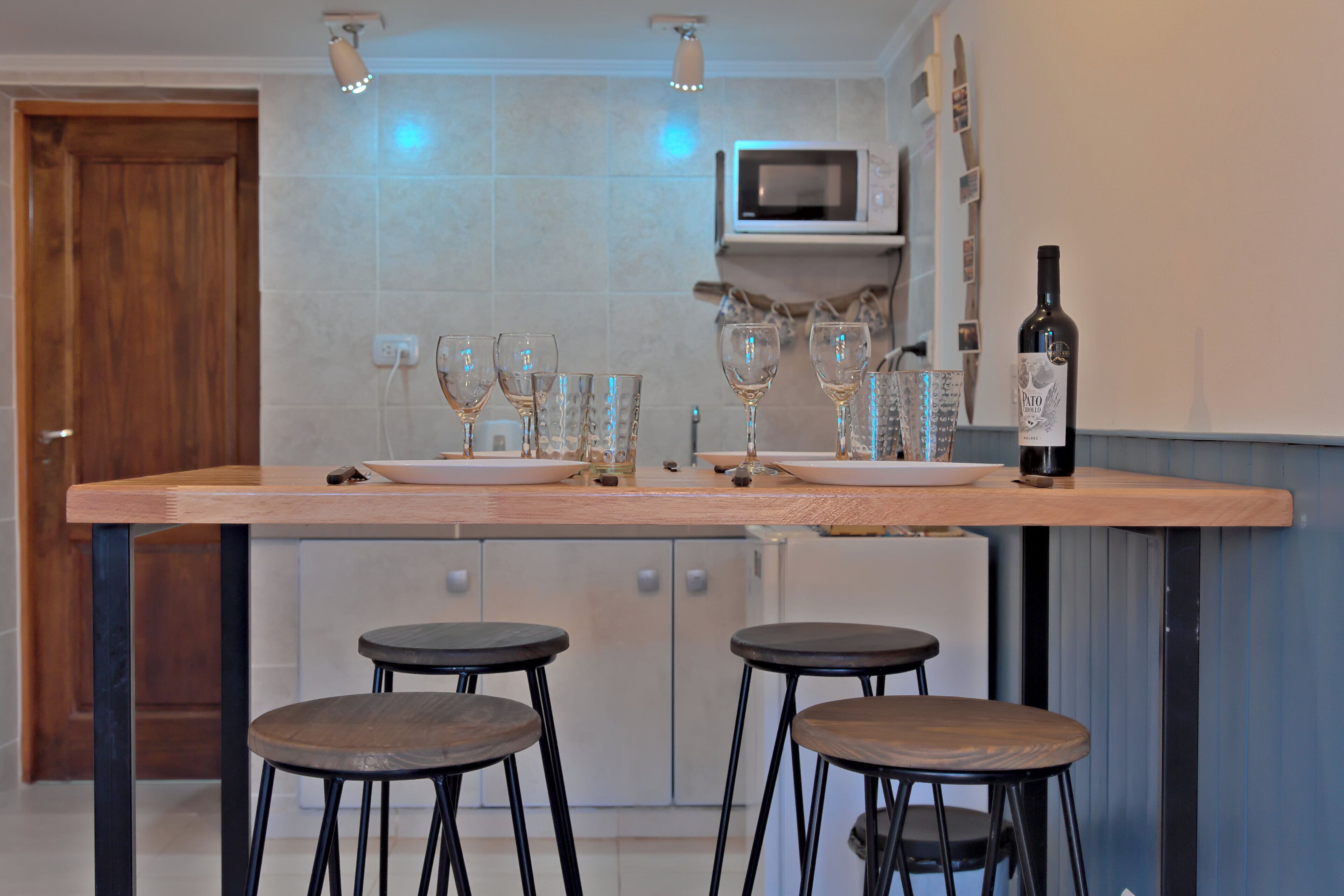 A kitchen with a wooden countertop, two stools, a wine bottle, and a microwave.