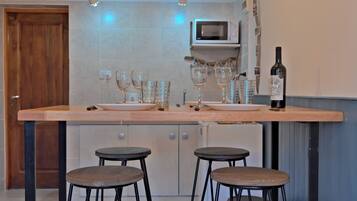 A kitchen with a wooden countertop, two stools, a wine bottle, and a microwave.