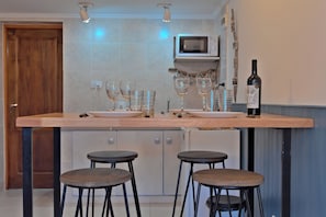 A kitchen with a wooden countertop, two stools, a wine bottle, and a microwave.