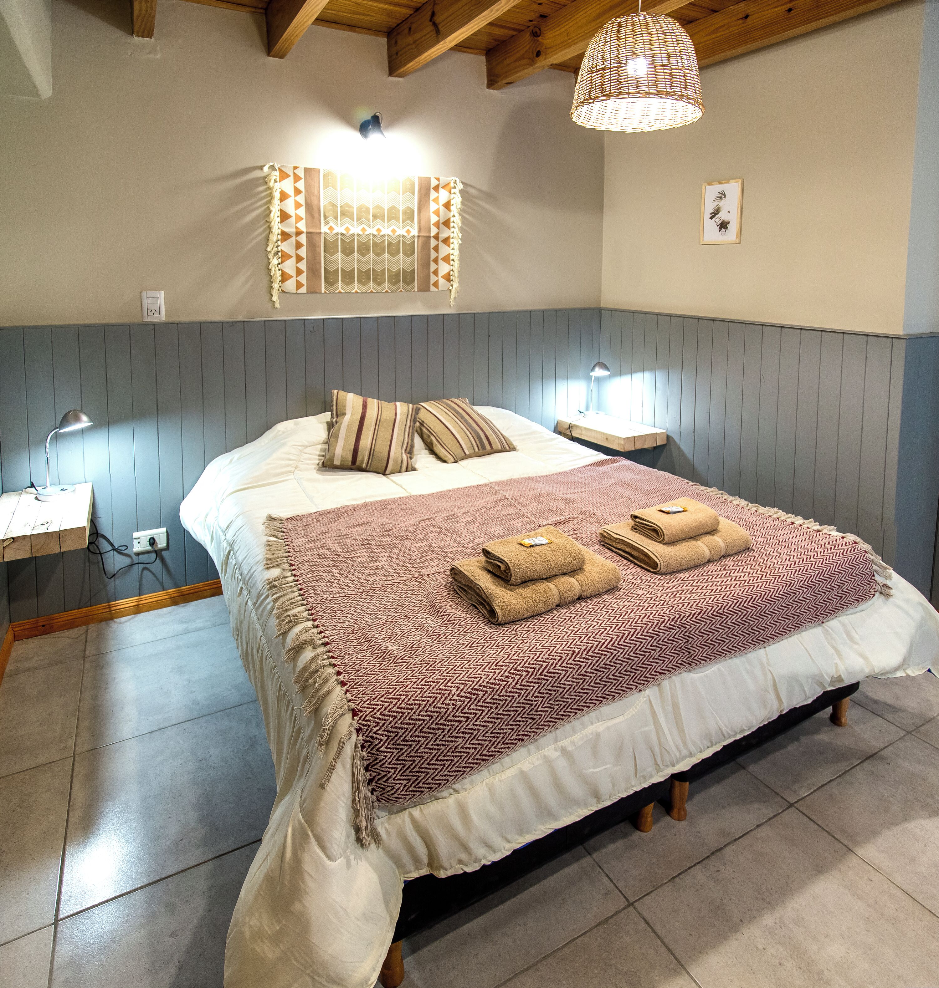 A bedroom with a bed, bedside lamps, a wall-mounted light fixture, and a framed picture.