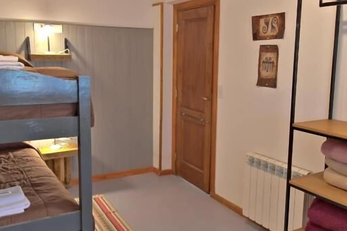 Habitació amb un llit superposat, sostre de fusta, una porta, un radiador i una estant amb tovalloles.