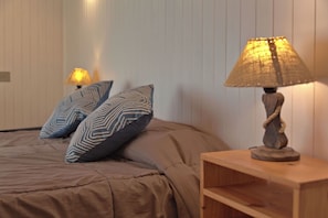 A bedroom with a bed, two patterned pillows, a bedside lamp, and a wooden nightstand.