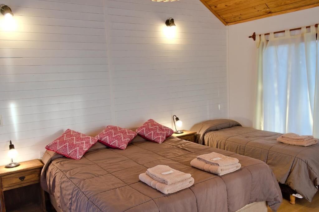 A bedroom with two beds, each with a brown bedspread, a nightstand with a lamp, and a window with curtains.
