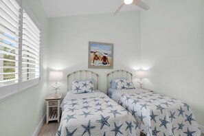 Ein Schlafzimmer mit zwei Betten, sternenmuster-Bettwäsche, einem Strandbild und einem Deckenventilator.