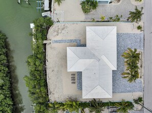Eine Luftaufnahme eines Anwesens direkt am Strand mit einer großen, offenen Terrasse, einem Pool und einem Bootssteg.