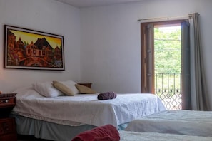 A bedroom with two beds, a painting on the wall, and a balcony with a metal railing.