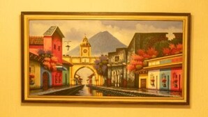 Un tableau encadré représentant une scène de ville avec un pont, des bâtiments et des montagnes.