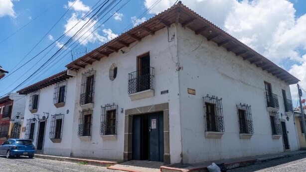 Un edificio de dos pisos con fachada blanca, múltiples ventanas con rejas y un techo de tejas rojas.