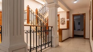 Un couloir avec un escalier, des colonnes blanches et une porte donnant sur une chambre à coucher.
