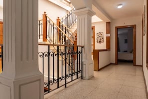 Un pasillo con una escalera, columnas blancas y una puerta que da a un dormitorio.
