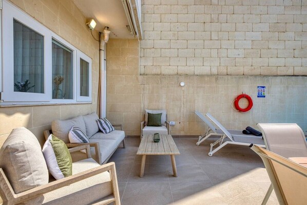 Une terrasse extérieure aménagée avec un canapé, des chaises, une table et un espace près de la piscine équipé d’une bouée de sauvetage.