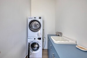 A compact laundry area with a front-loading washer and dryer, a small sink with a vanity, and a wooden floor.