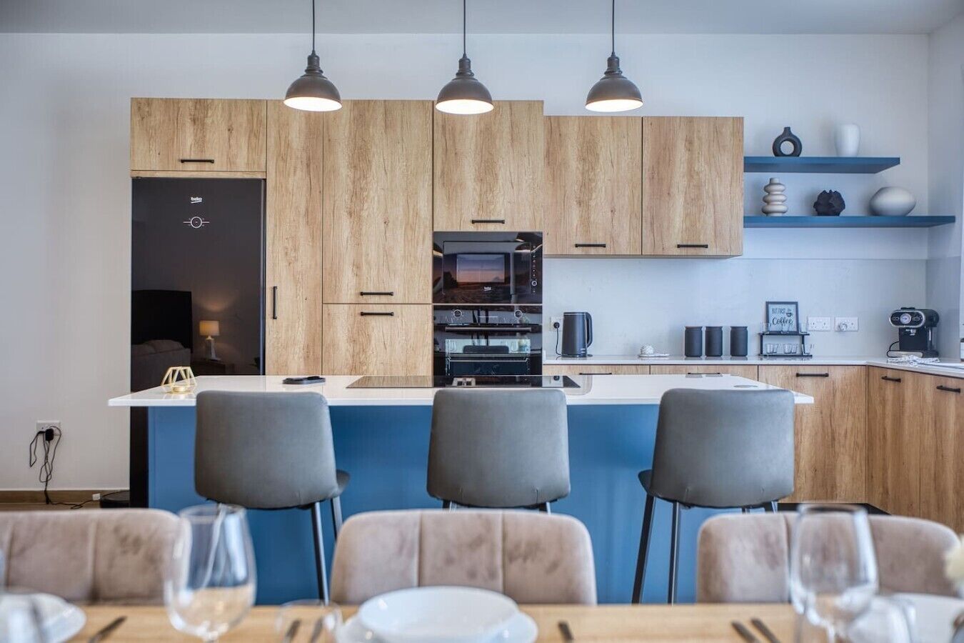 A modern kitchen with wooden cabinets, a central island, bar stools, and pendant lighting.